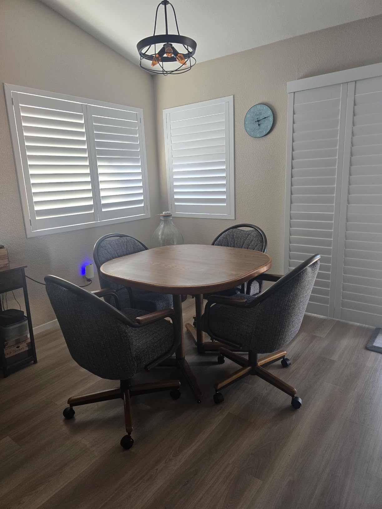 Round wood dining table and dark upholstered Chromcraft chairs beside white window shutters