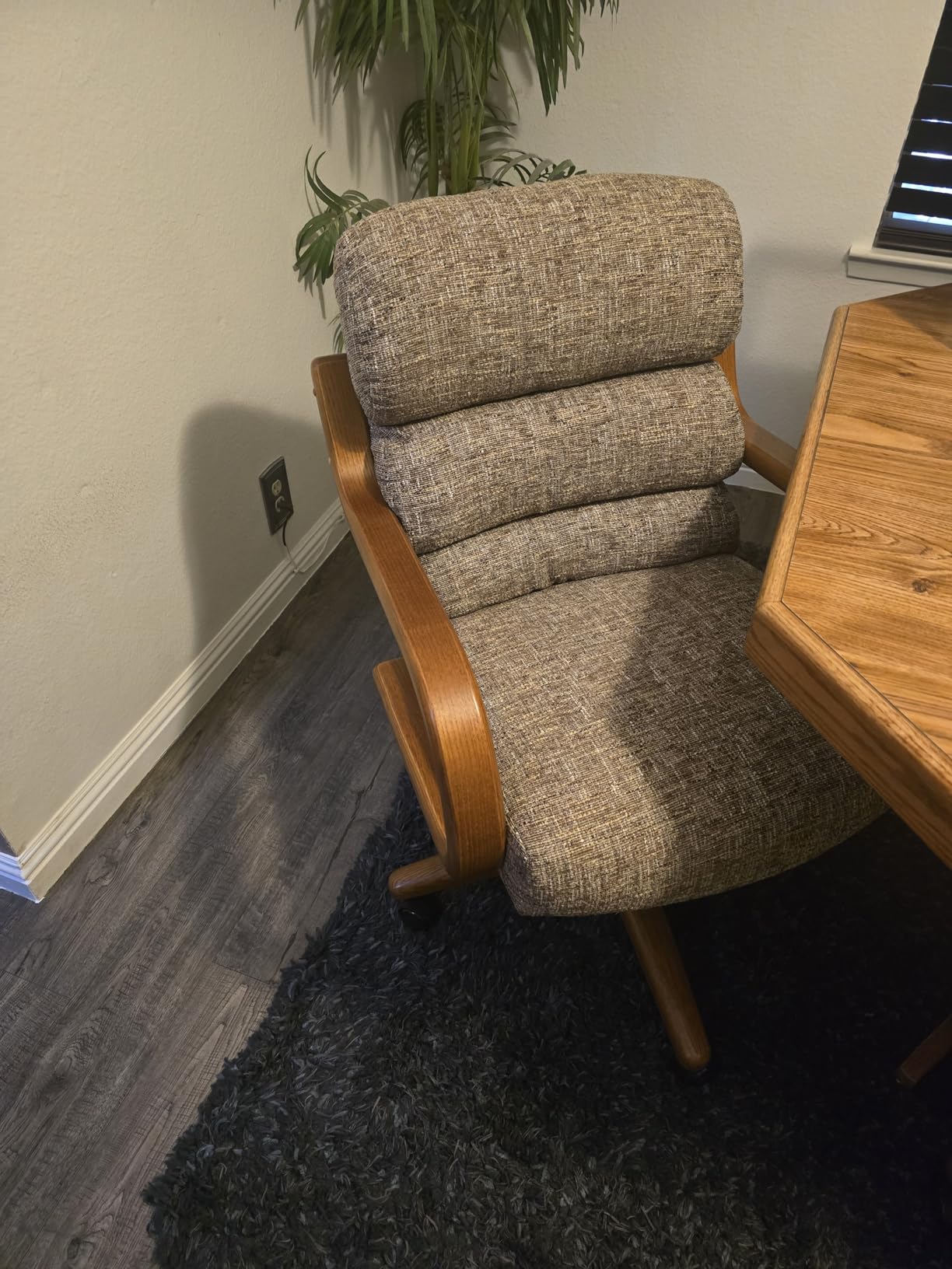 Close-up of a textured upholstered Chromcraft chair with wood arms beside a dining table